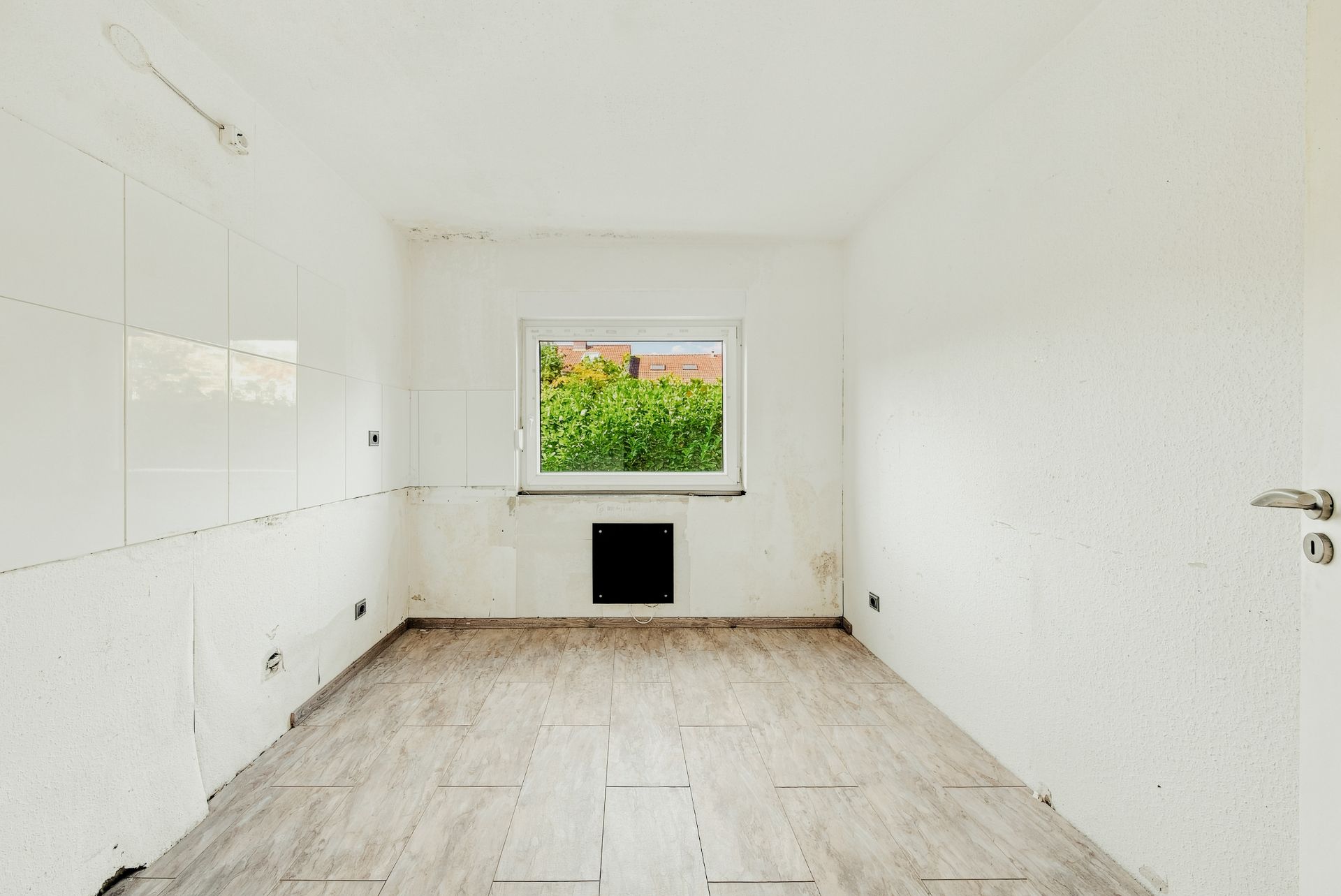 Leerer Raum mit Fliesenboden und einem Fenster, weiße Wände, kein Mobiliar.