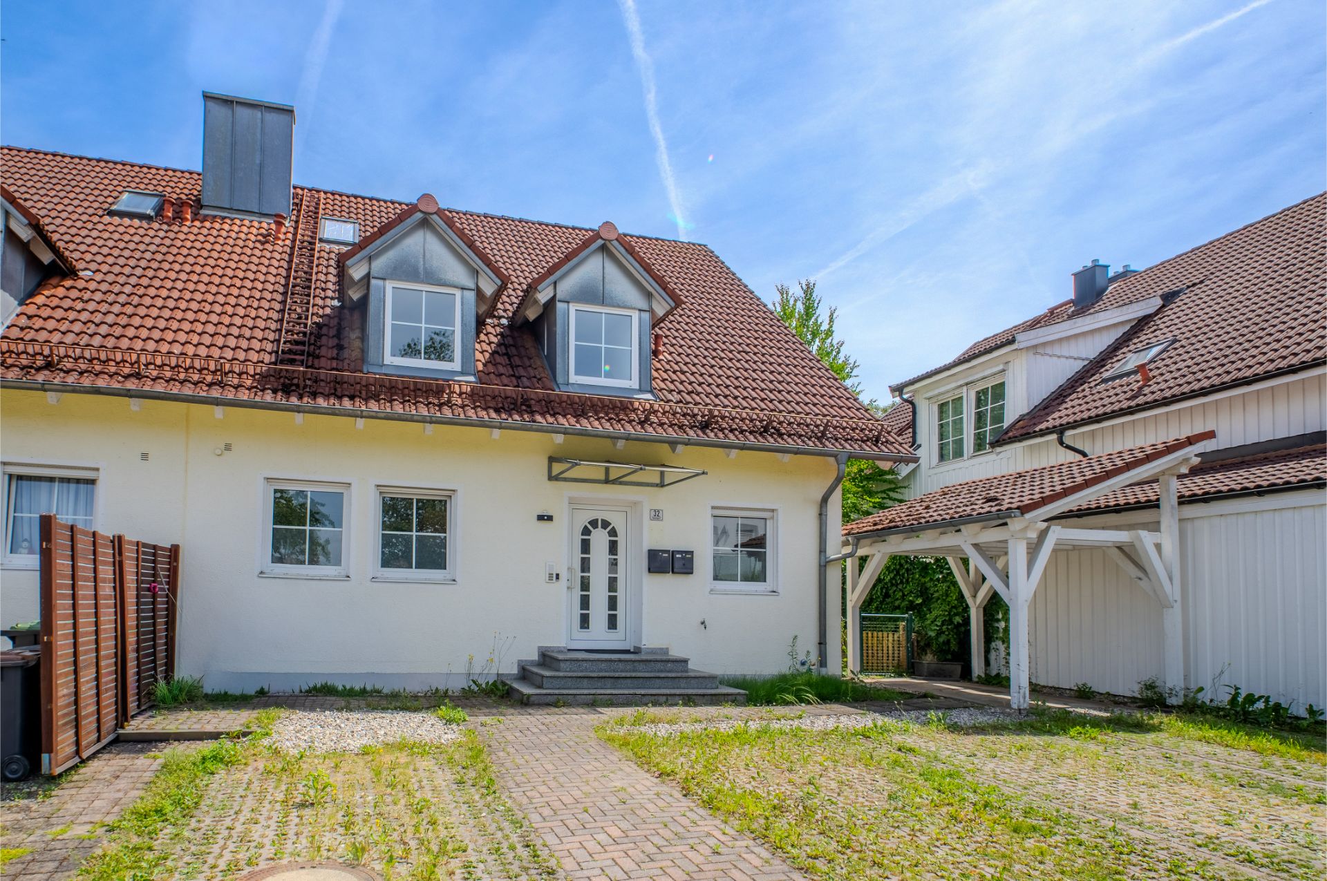 Zweistöckiges Wohnhaus mit rotem Dach, Vorgarten und angrenzendem Carport bei Tageslicht.