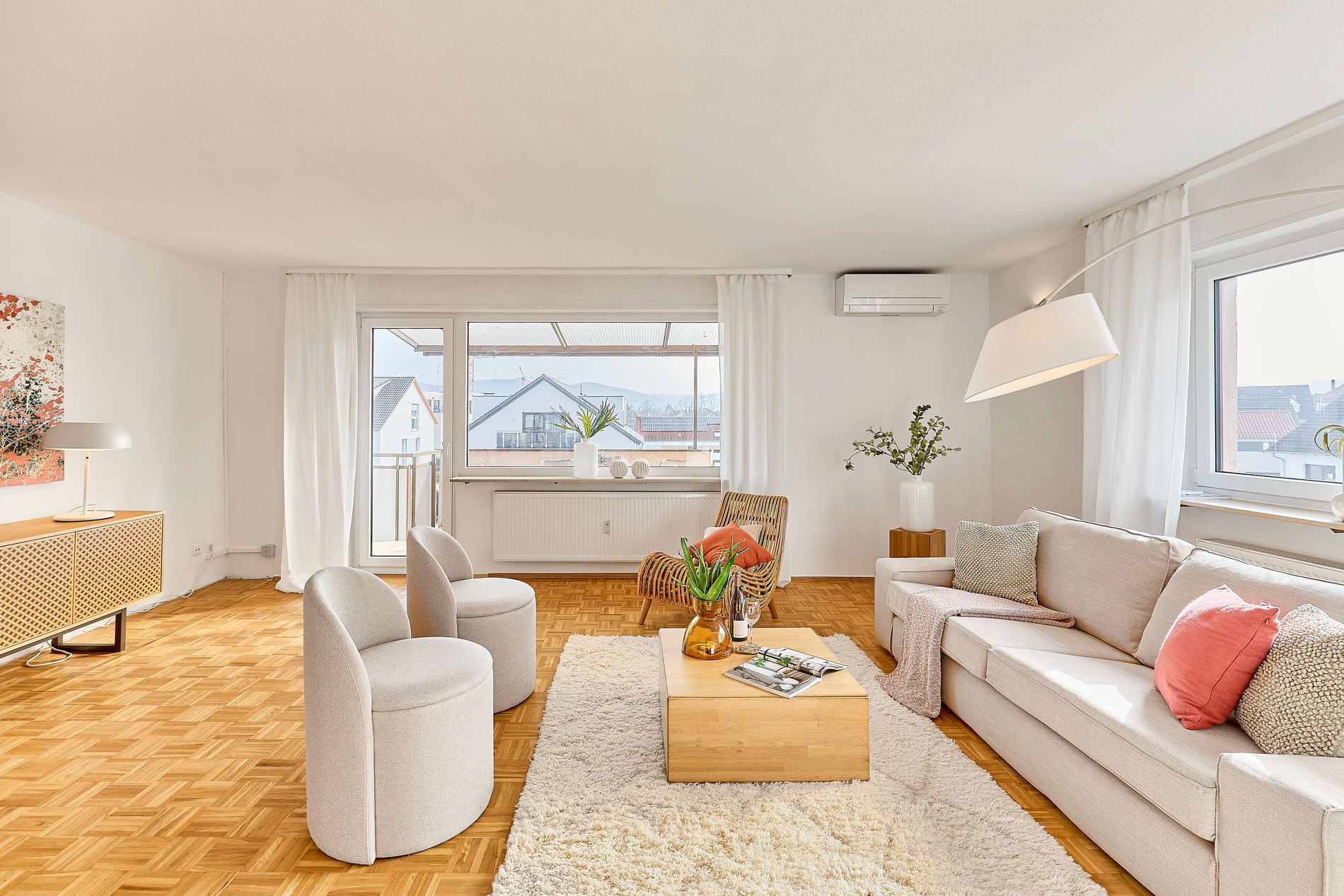 Helles Wohnzimmer mit Sofa, Sesseln, Couchtisch, großem Fenster und Holzboden.