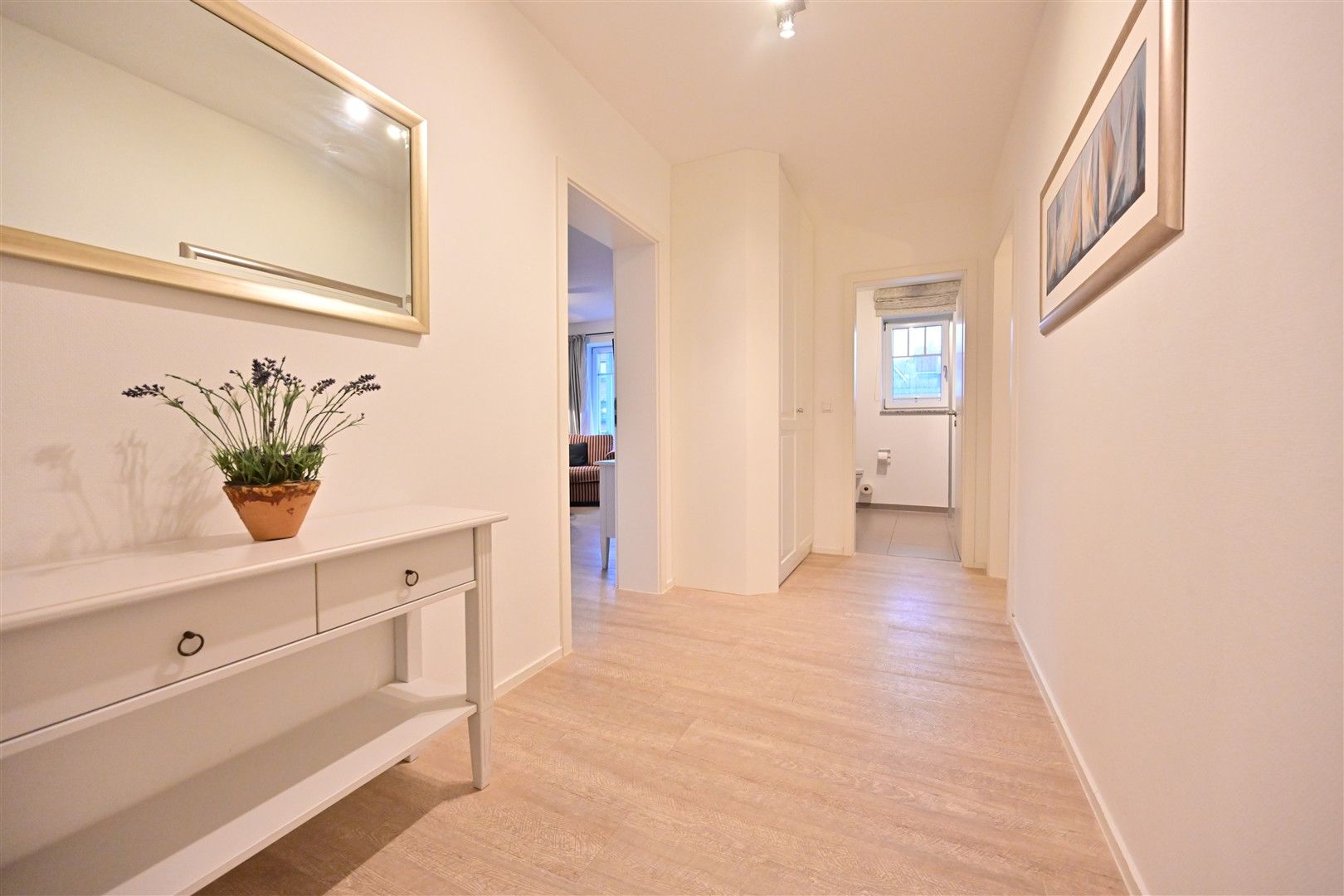 Heller Flur mit weißem Sideboard, Spiegel, Pflanze und Bildern an den Wänden.