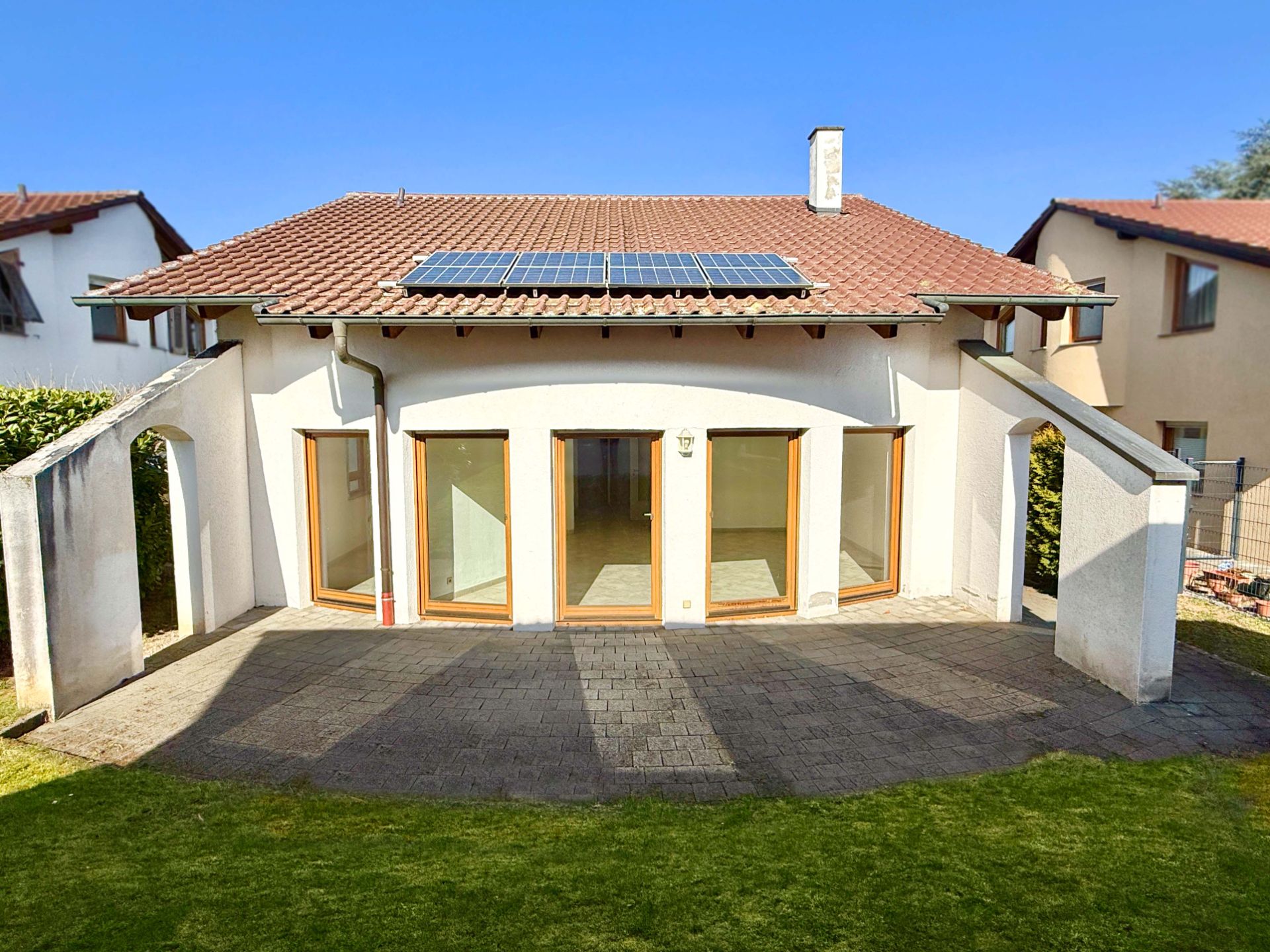 Einfamilienhaus mit Solarpanels, Terrasse und großen Fenstern im Gartenbereich.