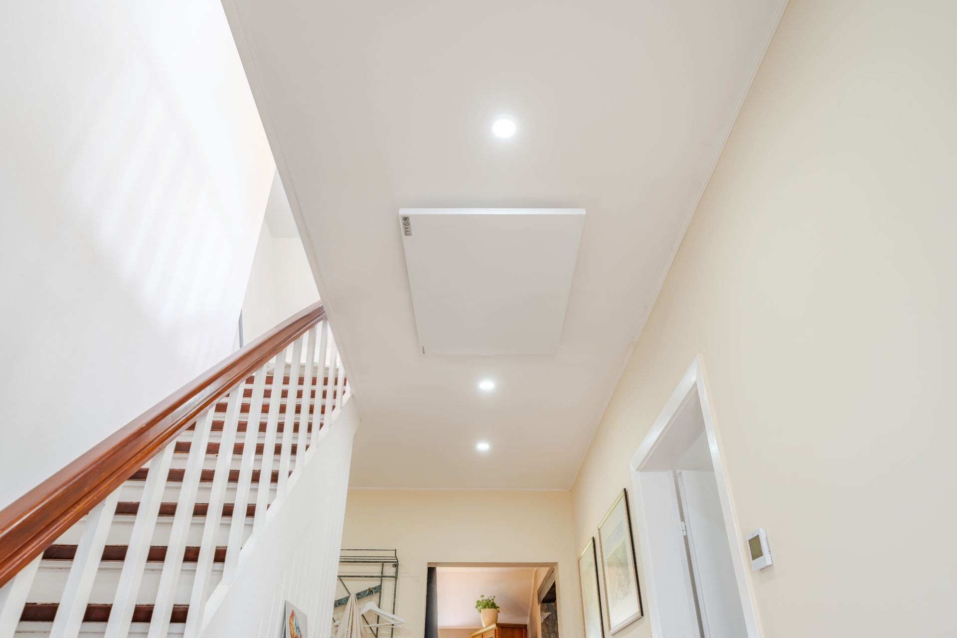 Treppe mit Holzgeländer in einem hellen Flur, Decke mit Einbaulampen.