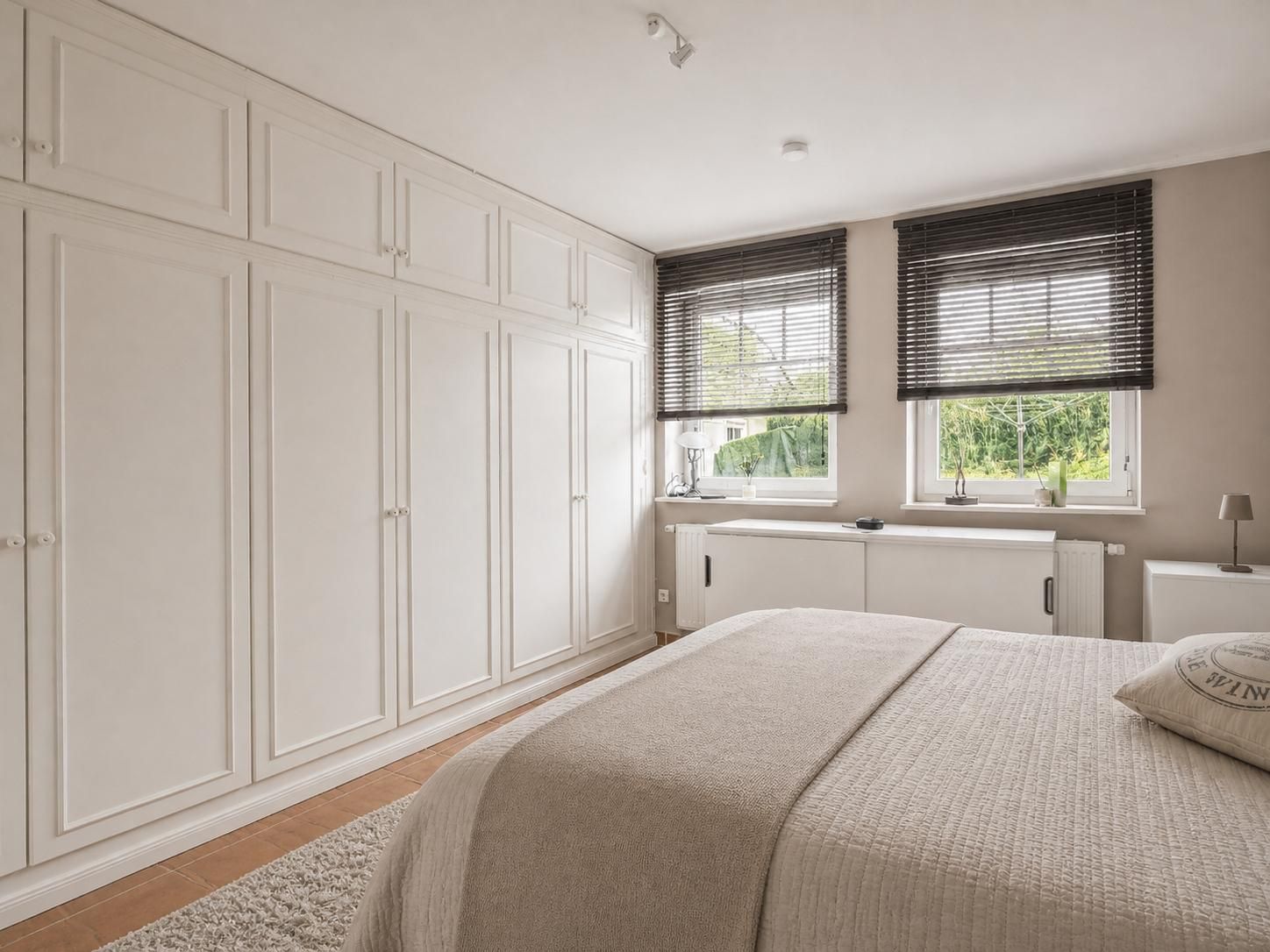 Helles Schlafzimmer mit großem Einbauschrank, Doppelbett und zwei Fenstern mit Jalousien.