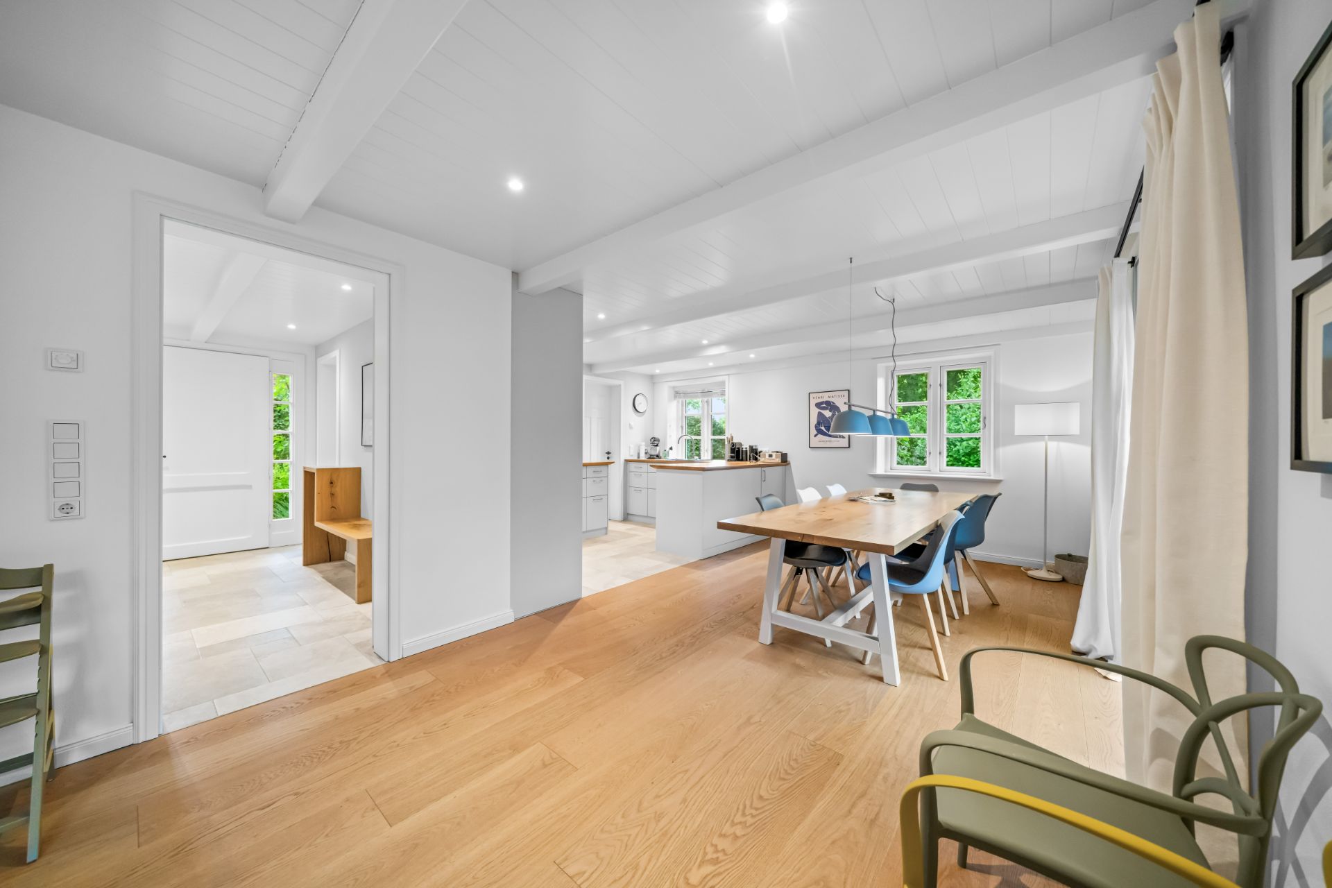 Helles Wohnzimmer mit Holzboden, Esstisch, Stühlen und großen Fenstern.