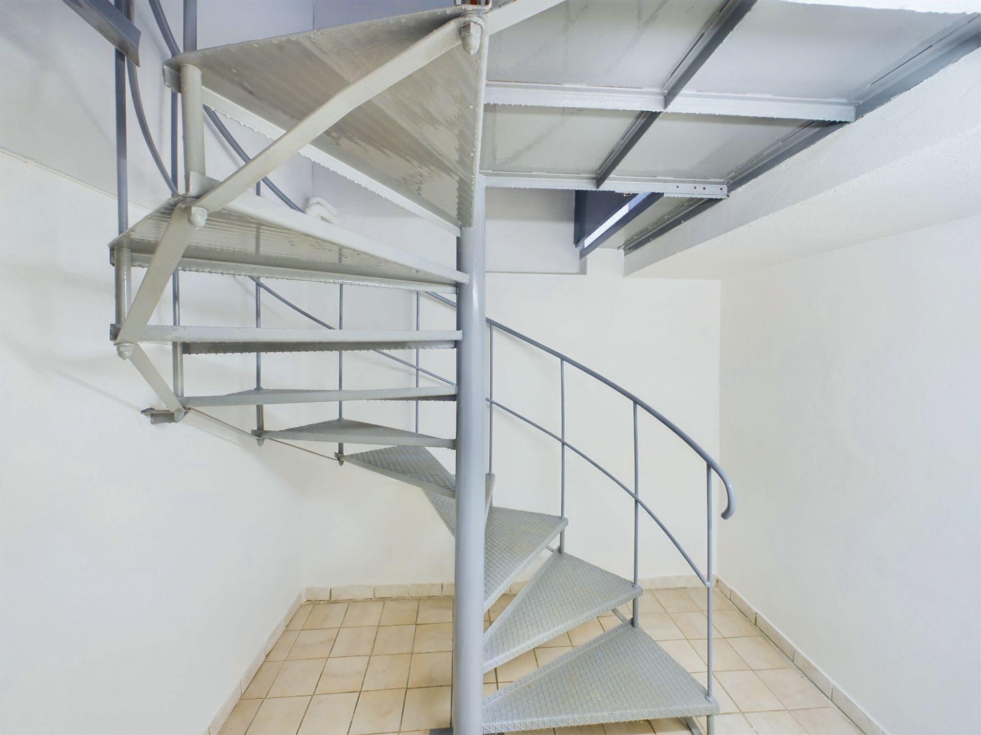 Metallwendeltreppe in einem weißen Raum mit Fliesenboden.