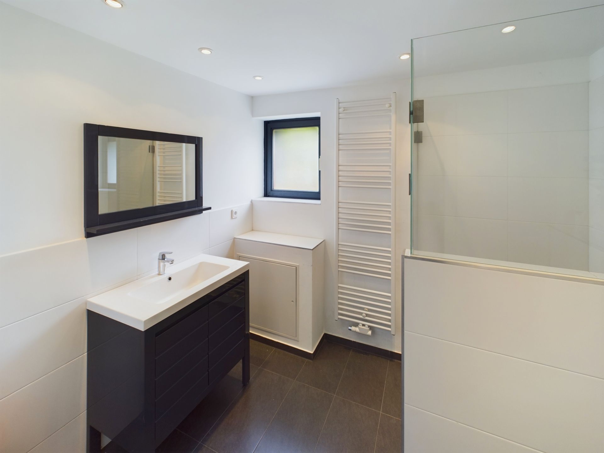 Modernes Badezimmer mit Waschbecken, Spiegel, Handtuchheizkörper und Glasdusche.