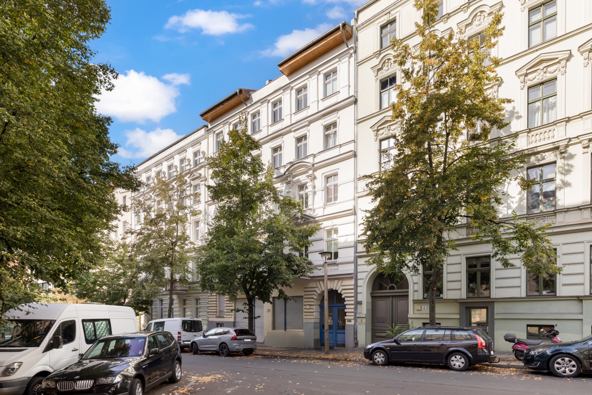Mehrstöckiges Wohnhaus mit Bäumen entlang der Straße und geparkten Autos davor.