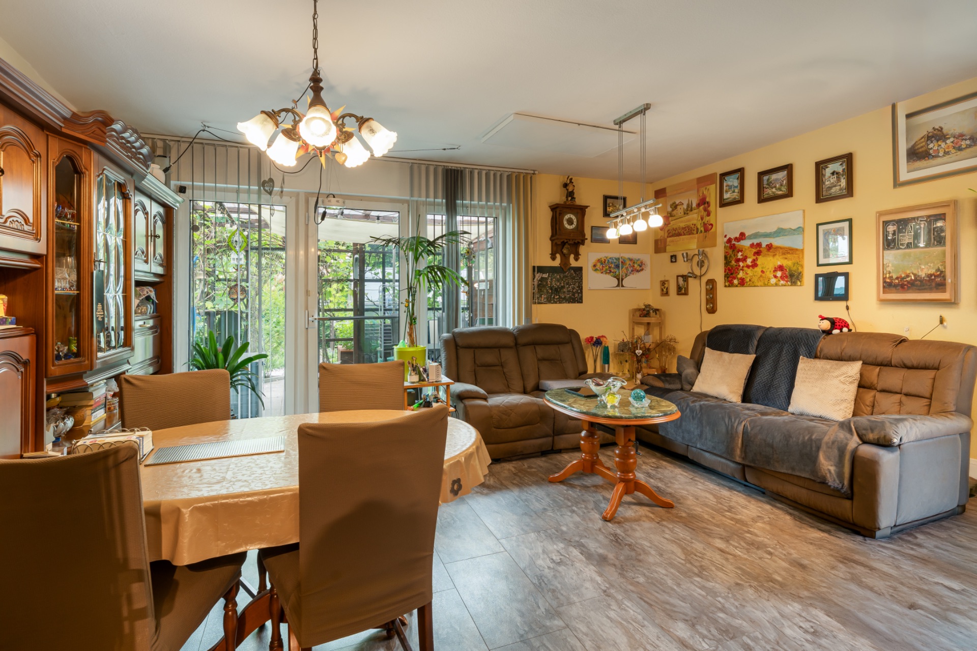 Gemütliches Wohnzimmer mit Esstisch, Sofas, Wandbildern und großen Fenstern zum Garten.