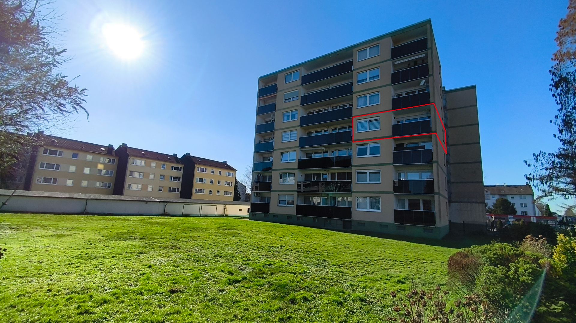 Mehrstöckiges Wohnhaus mit vielen Fenstern und großem grünen Rasen im Vordergrund.