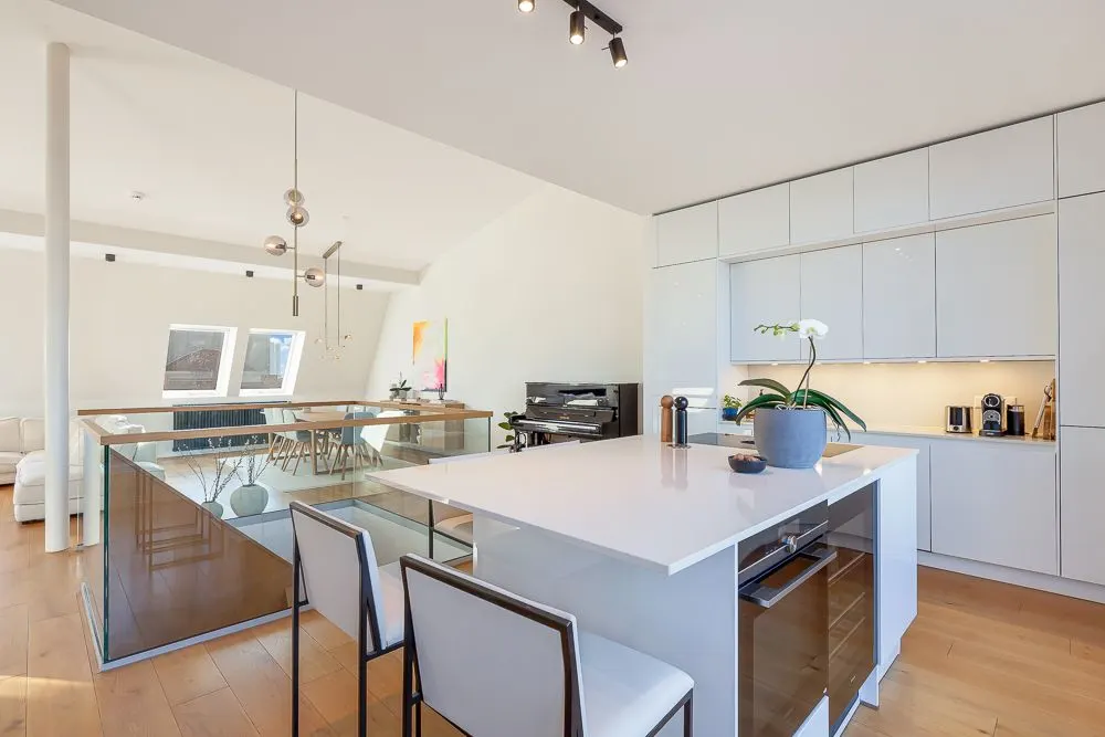 Moderne Küche mit Kochinsel, weißen Schränken und Essbereich im Hintergrund.