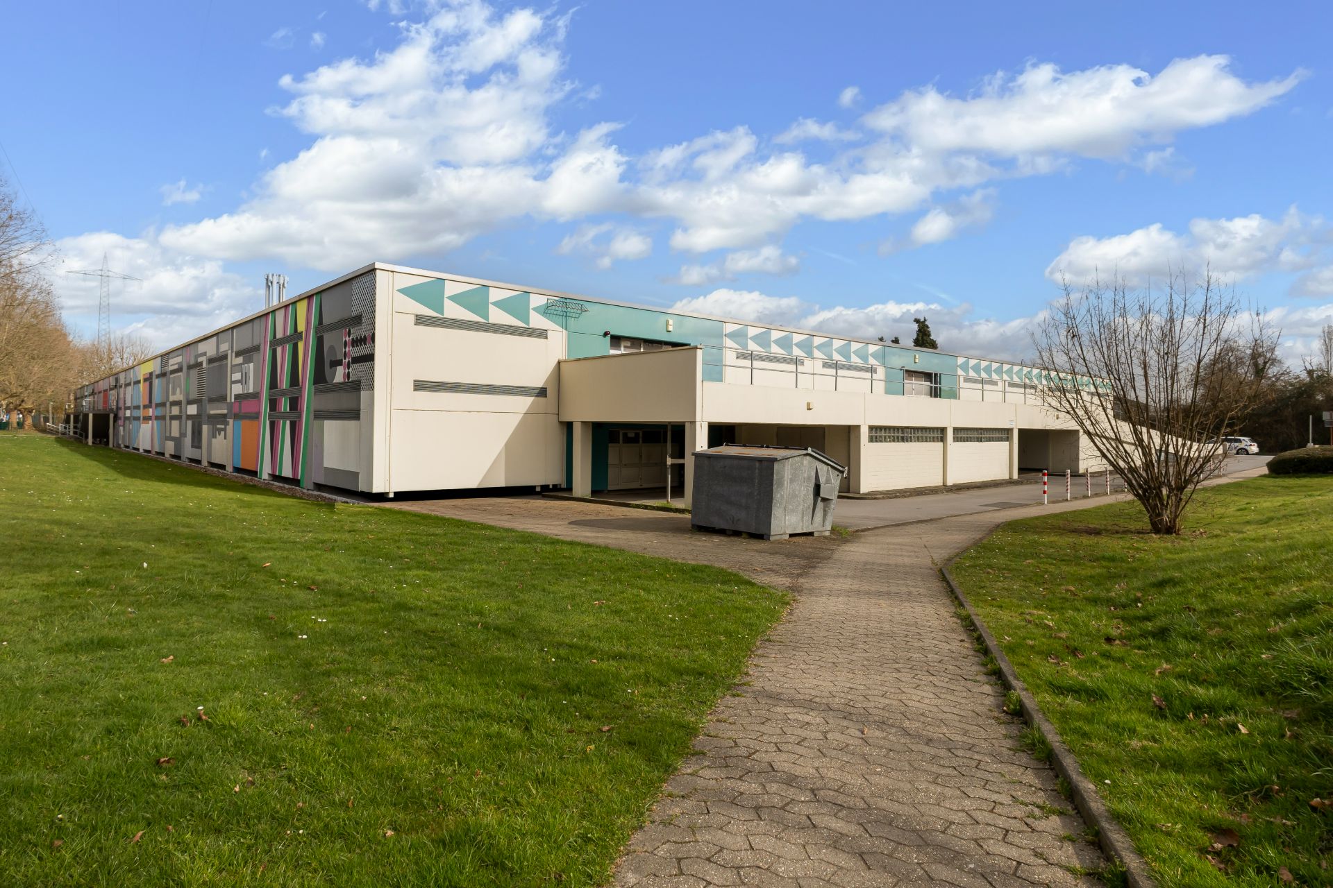 Flaches Wohngebäude mit bunten Fassadenelementen und Gehweg im Vordergrund.
