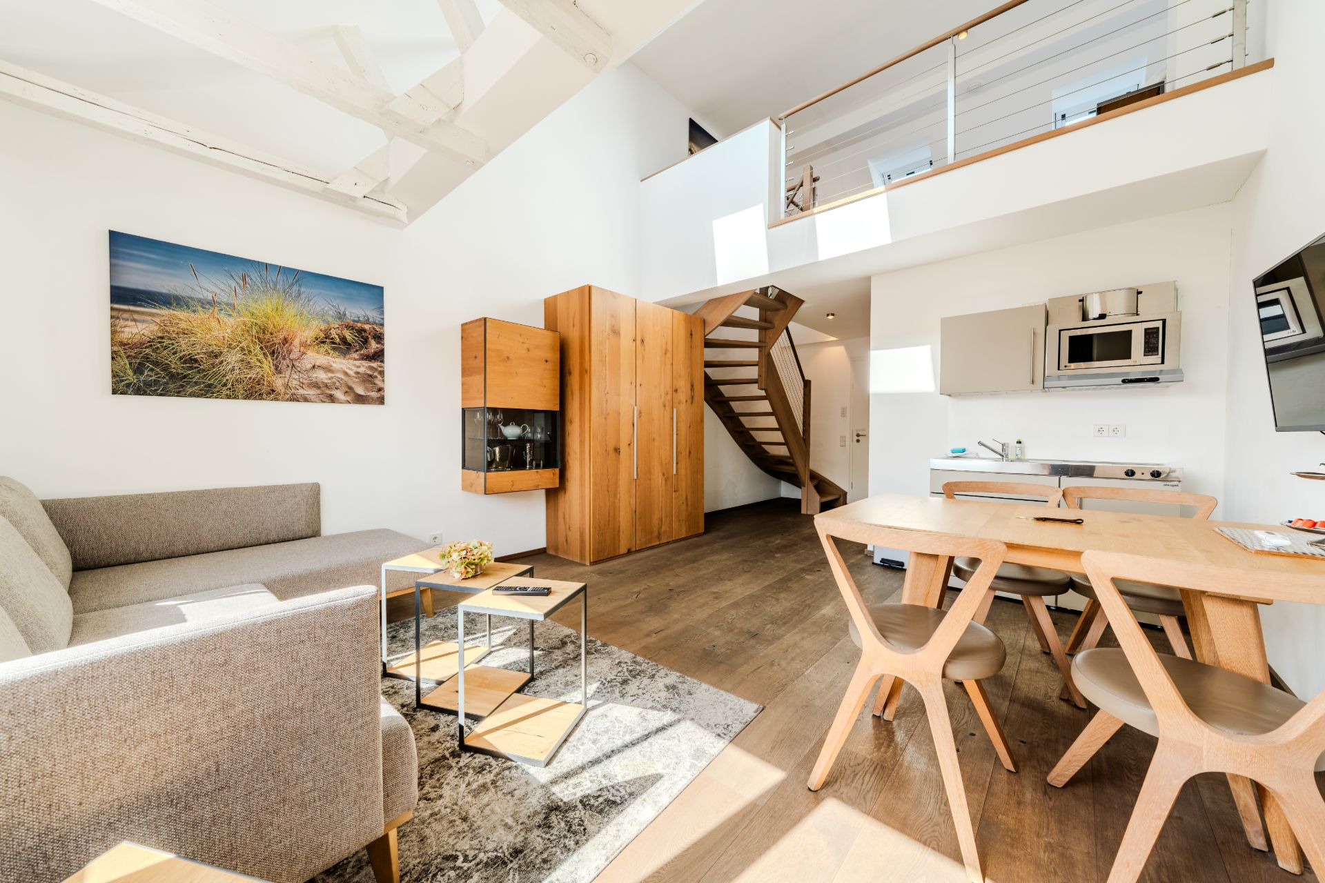 Helles Wohnzimmer mit Sofa, Esstisch, Küchenzeile, Holztreppe und Galerie.
