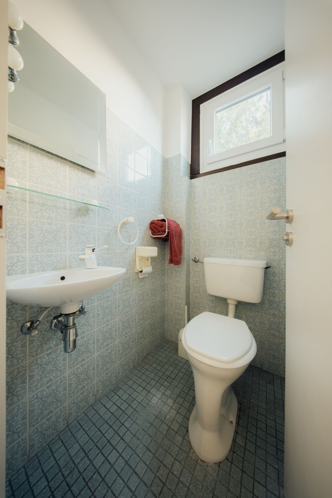 Kleines Badezimmer mit Toilette, Waschbecken, Spiegel und Fenster.