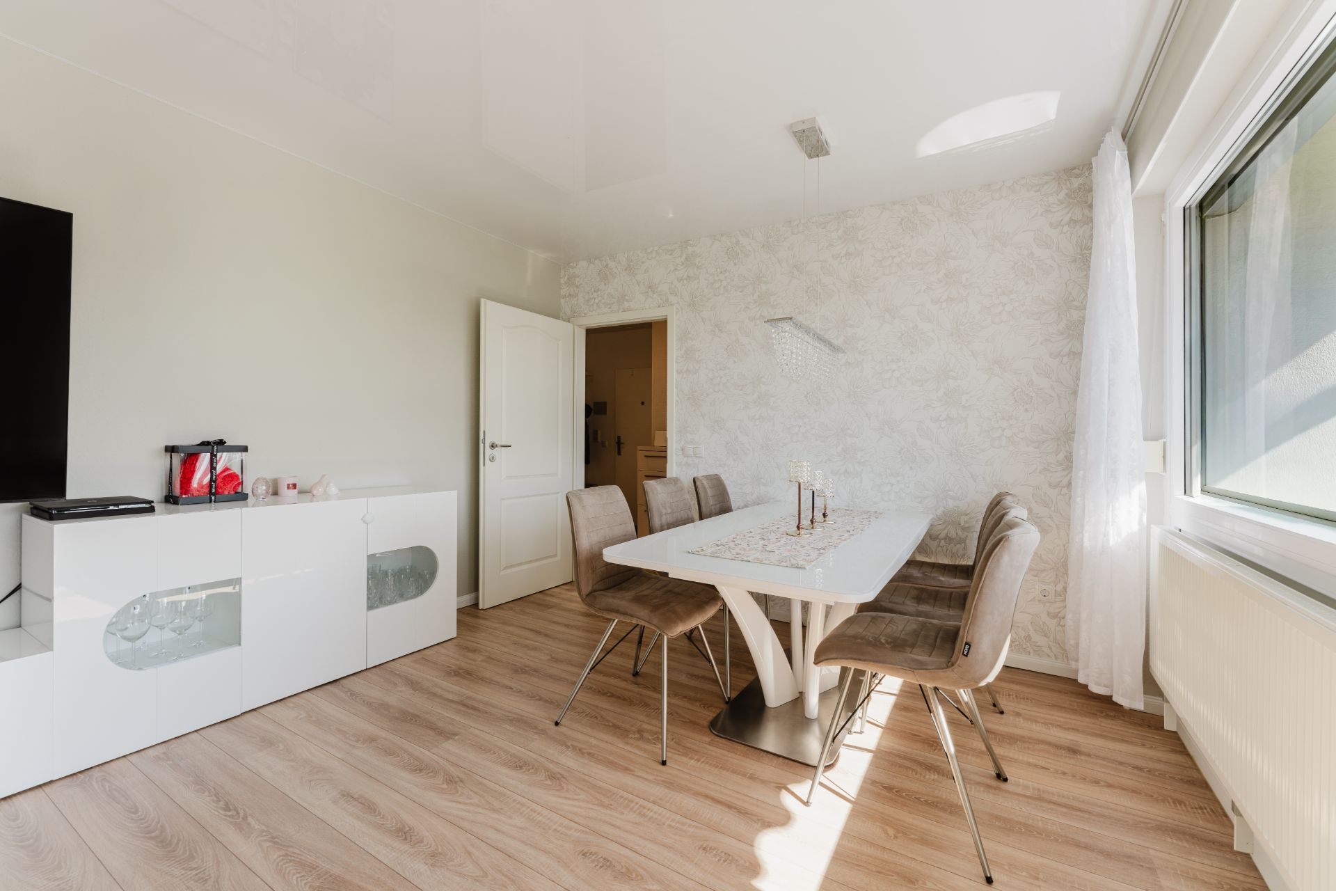 Helles Esszimmer mit weißem Tisch, sechs Stühlen, Sideboard und großem Fenster.