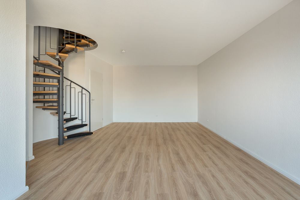 Leerer Raum mit Holzfußboden und Wendeltreppe aus Metall in der Ecke.
