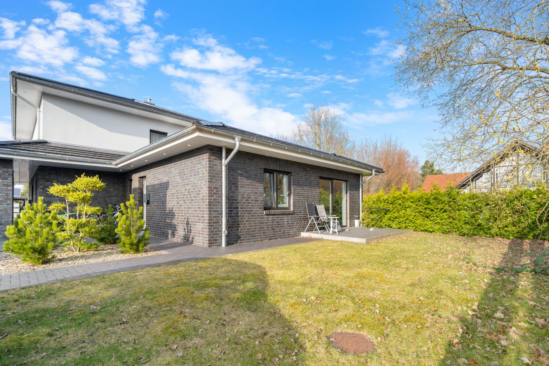 Einfamilienhaus mit Terrasse, Garten und Gartenmöbeln an einem sonnigen Tag.