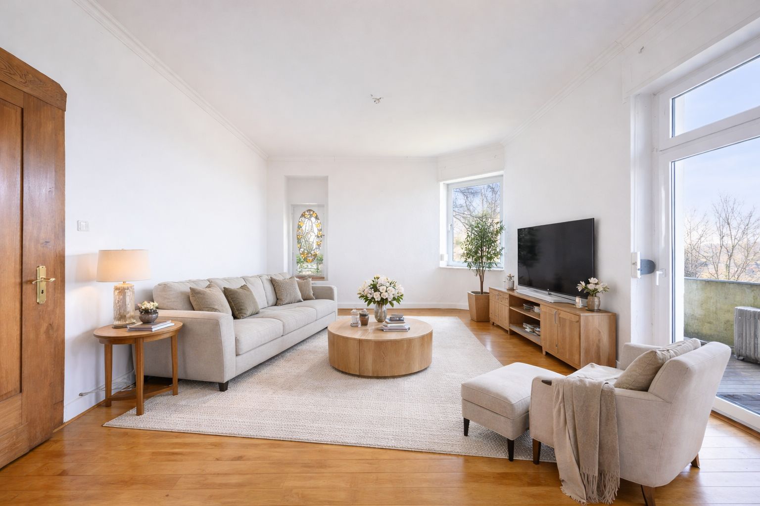 Helles Wohnzimmer mit Sofa, Sessel, Couchtisch, Fernseher und großen Fenstern.