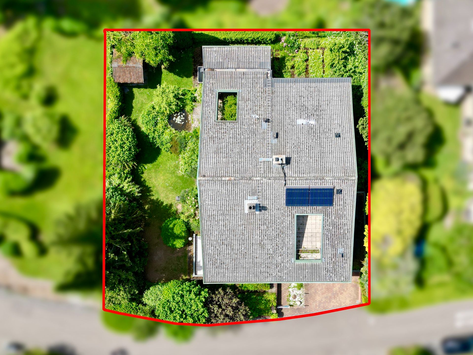 Luftaufnahme eines Wohnhauses mit grauem Dach, umgeben von Garten und Bäumen, Grundstück rot umrandet.