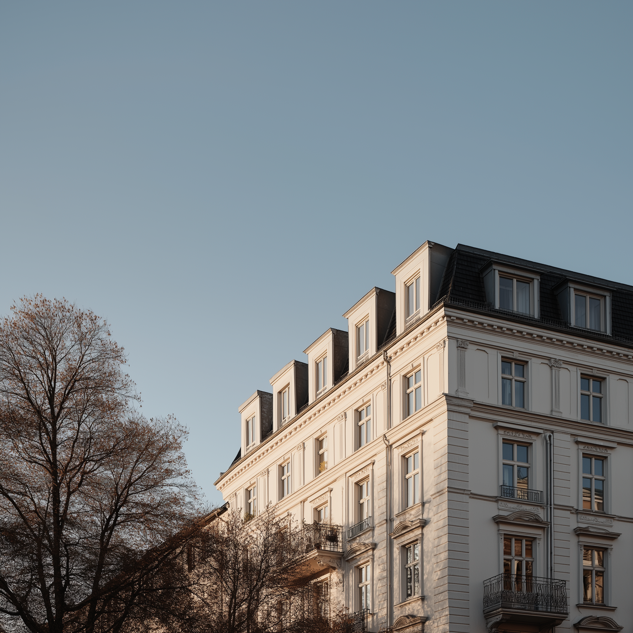 Modernes Wohnhaus mit mehreren Balkonen, umgeben von Bäumen, bei Sonnenschein.