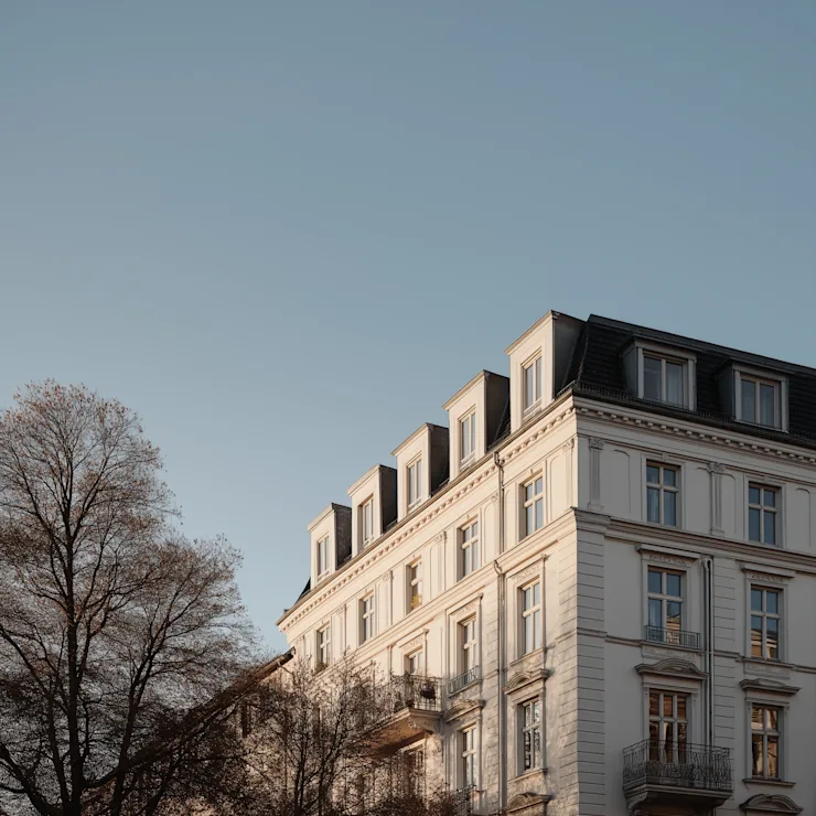 Modernes Wohnhaus mit mehreren Balkonen, umgeben von Bäumen, bei Sonnenschein.