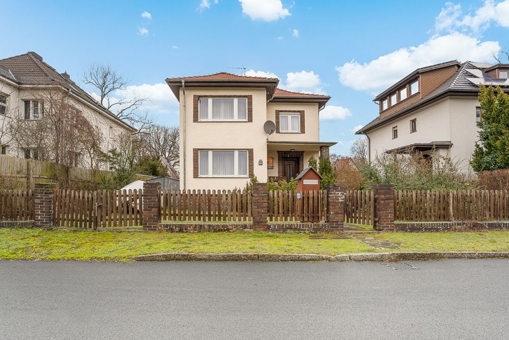 Zweistöckiges Einfamilienhaus mit braunem Zaun und Vorgarten an einer ruhigen Straße.