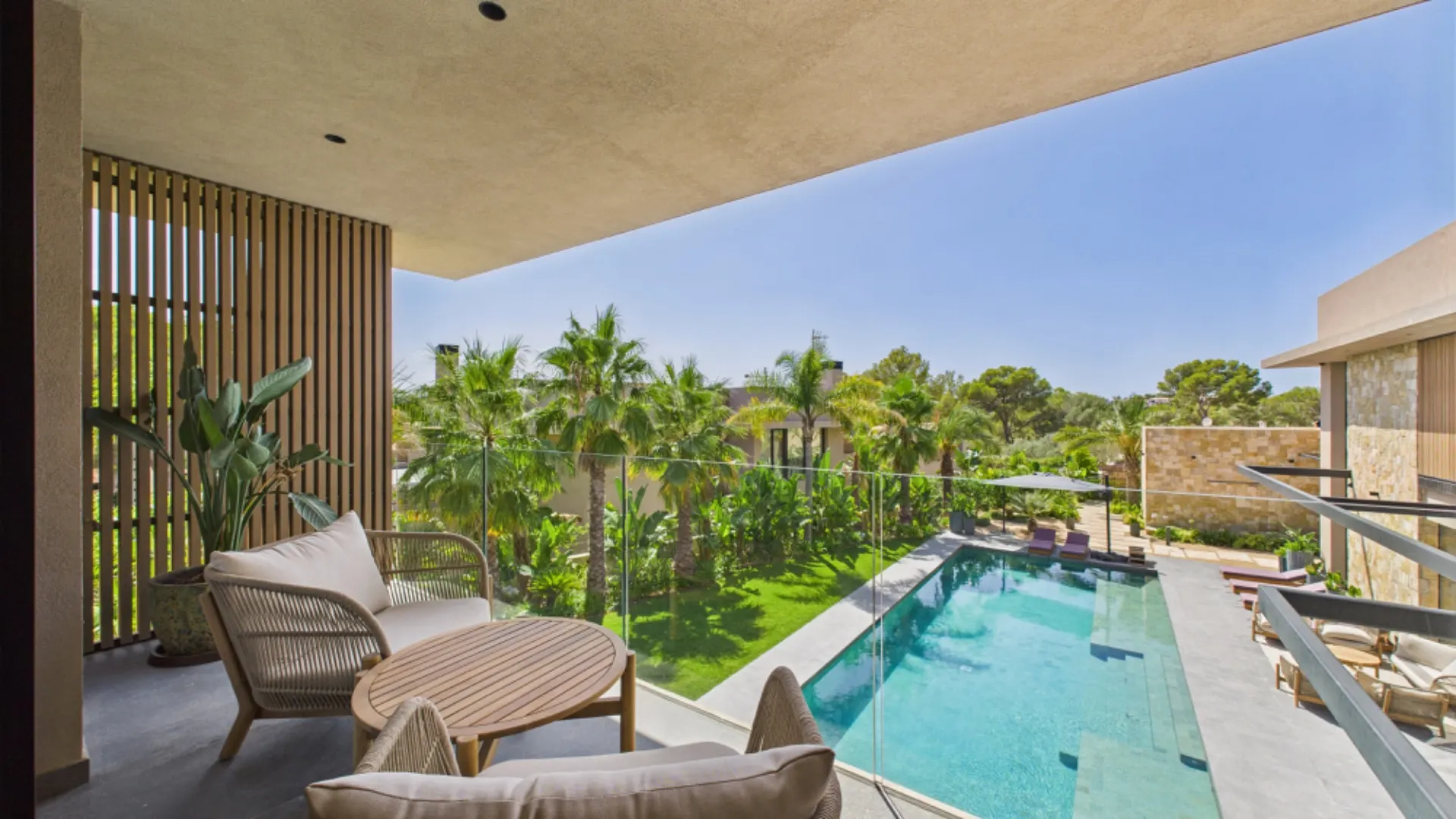 Balkon mit Sitzmöbeln und Blick auf einen Pool, umgeben von Palmen und Grünflächen.