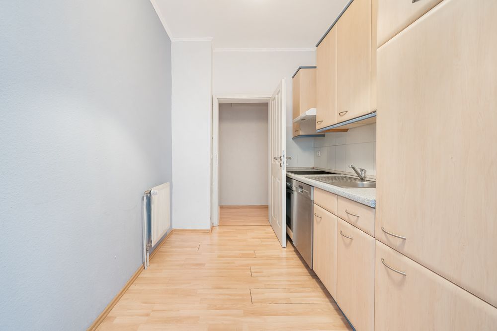 Helle Küche mit Holzschränken, Spüle und offen stehender Tür zu einem angrenzenden Raum.