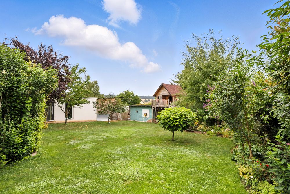 Großer, grüner Garten mit Bäumen, Sträuchern und zwei kleinen Gebäuden im Hintergrund.
