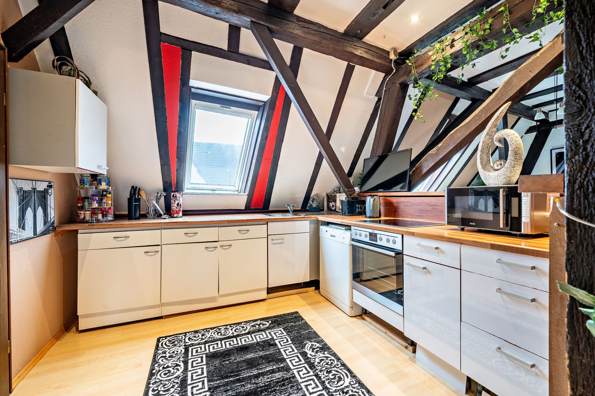 Moderne Küche mit Dachschräge, weißen Schränken und Holzbalken, Fenster in der Mitte.