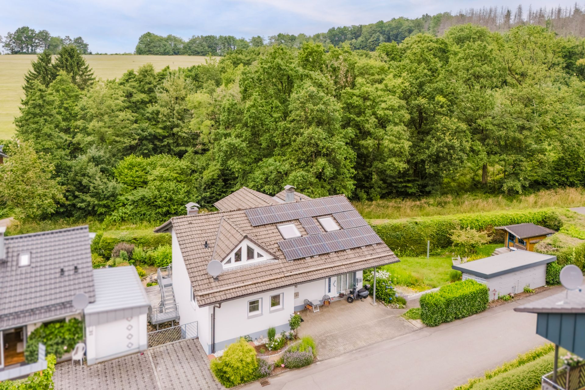 Haus mit Solarpanels auf dem Dach, umgeben von Bäumen und einer ruhigen Straße.