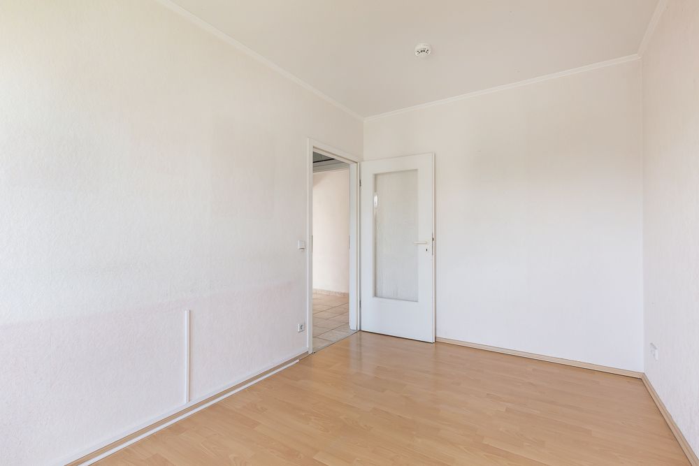 Leerer, heller Raum mit Holzboden und weißer Tür mit Glaseinsatz.