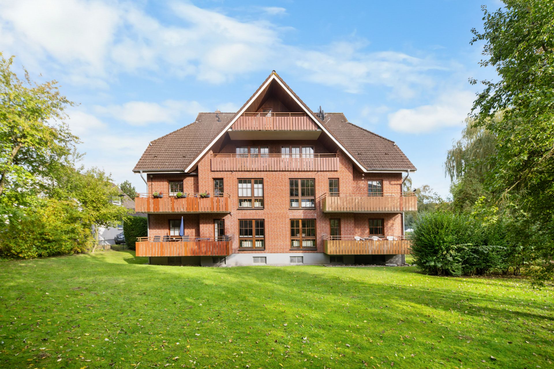 Mehrfamilienhaus mit Holzbalkonen und großem Garten, umgeben von Bäumen.