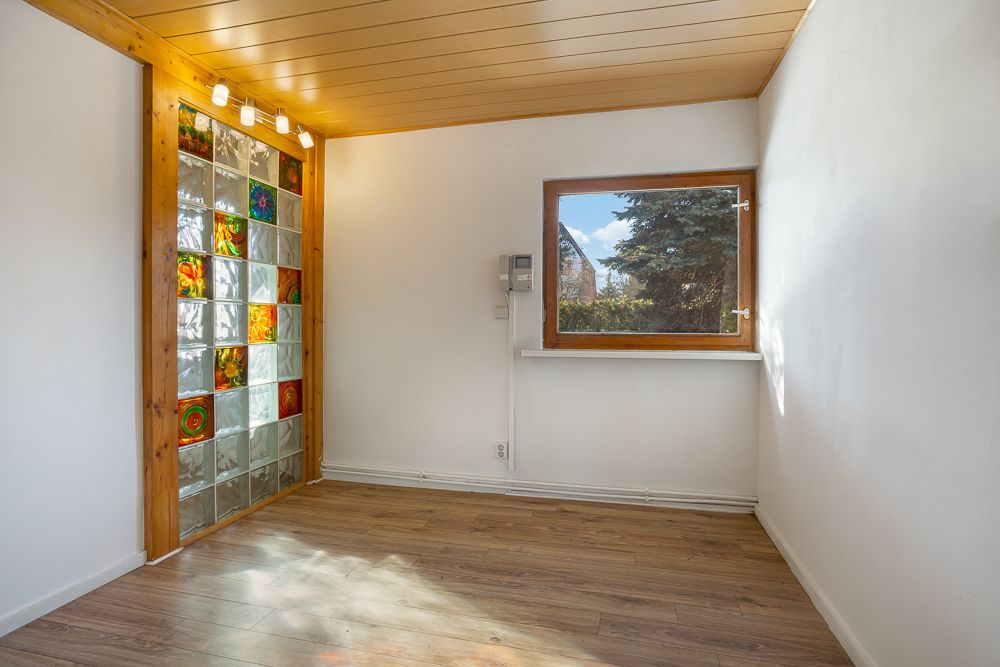 Heller Raum mit Holzdecke, Fenster und bunter Glaswand, Boden aus Holz.