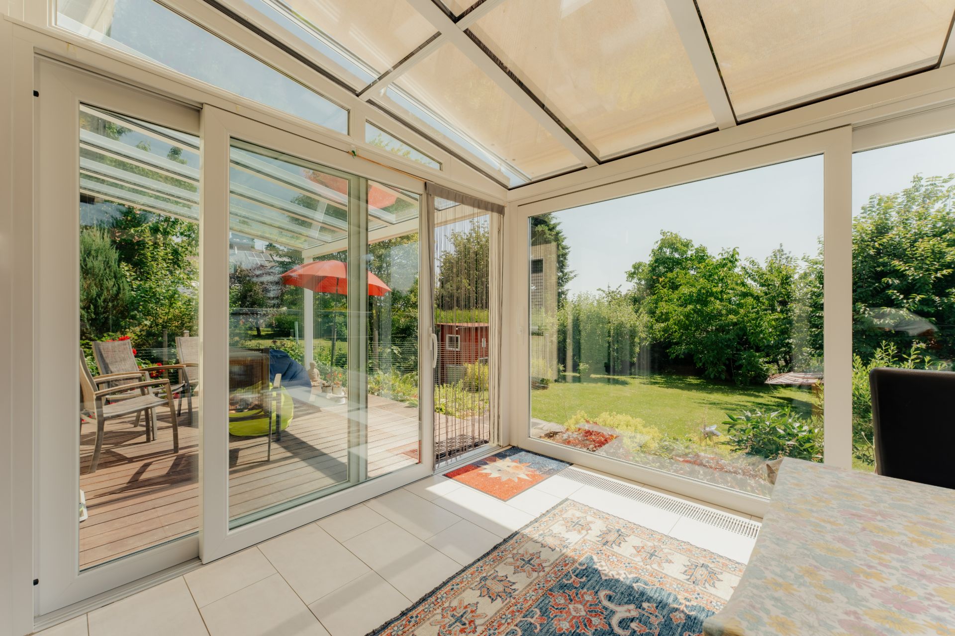 Wintergarten mit großen Fenstern, Blick auf Terrasse und grünen Garten.