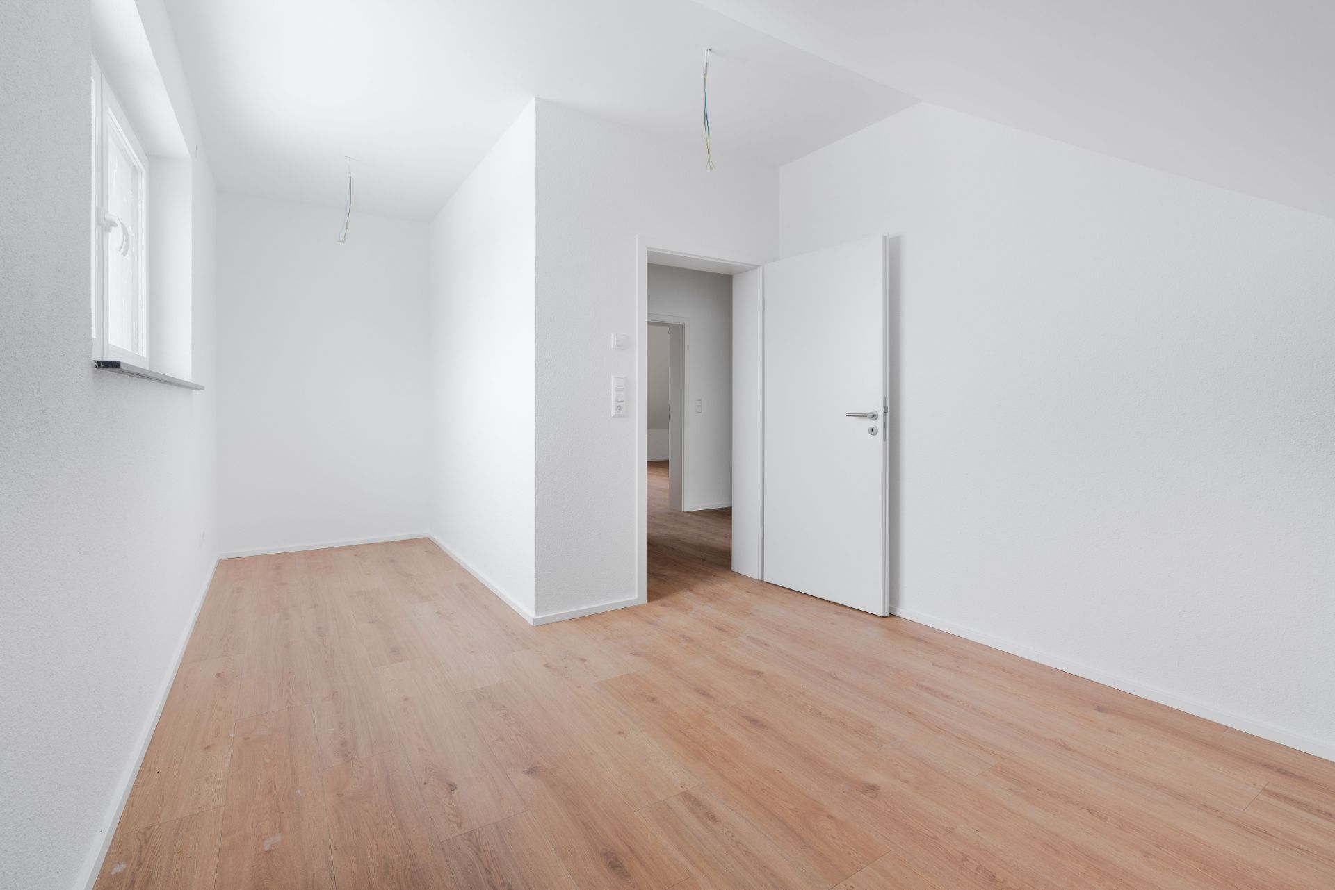 Heller leerer Raum mit weiß gestrichenen Wänden, Holzboden und einem offenen Fenster.