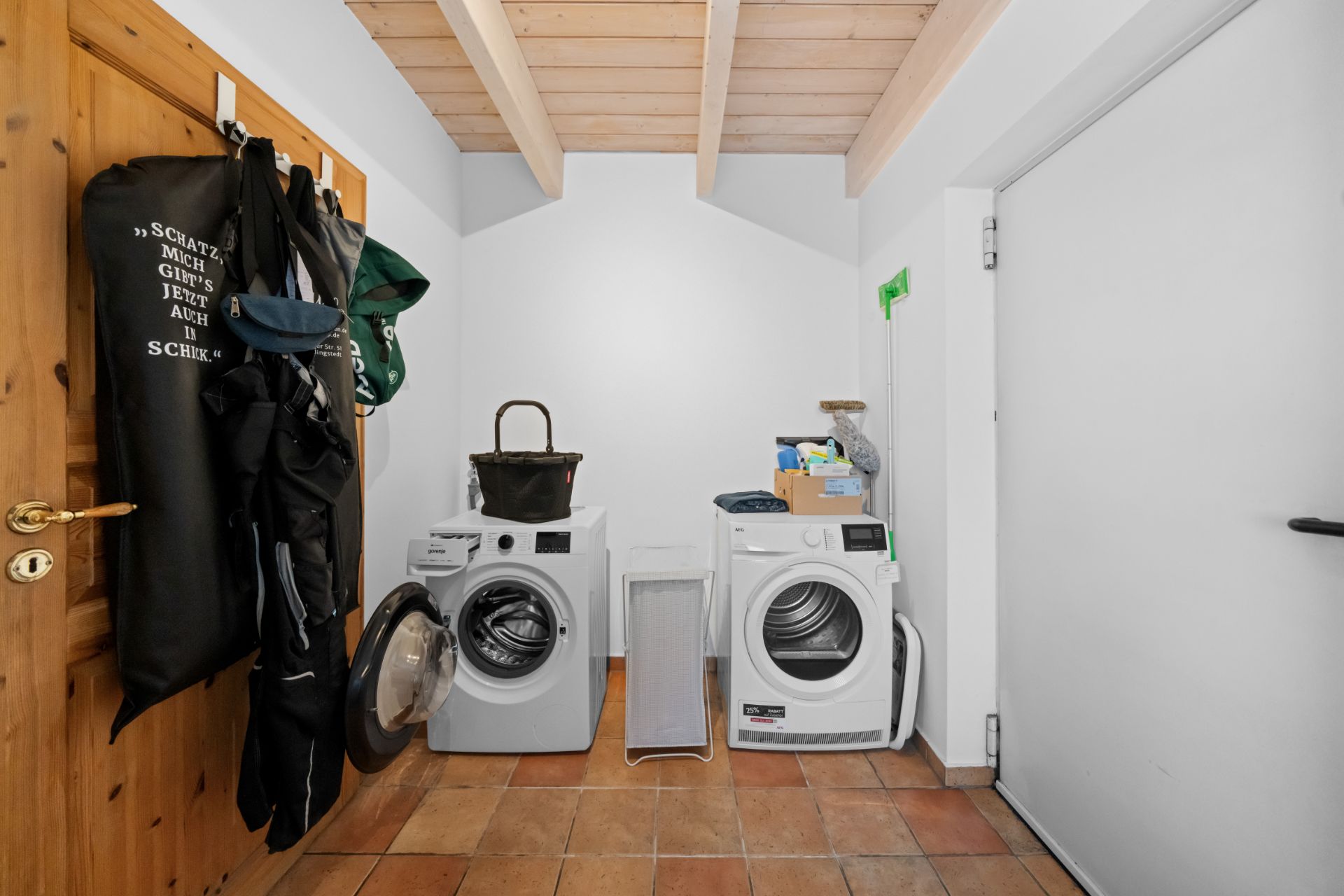 Hauswirtschaftsraum mit Waschmaschine, Trockner, Holztür und Kleiderhaken an der Wand.