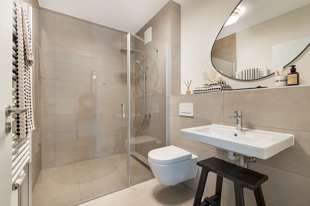 Modernes Badezimmer mit Dusche, WC, Waschbecken und großem Spiegel.