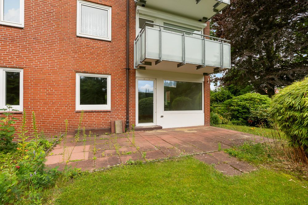Erdgeschoss eines roten Backsteinhauses mit Terrasse, Glastür und großem Fenster, daneben viel Grün.