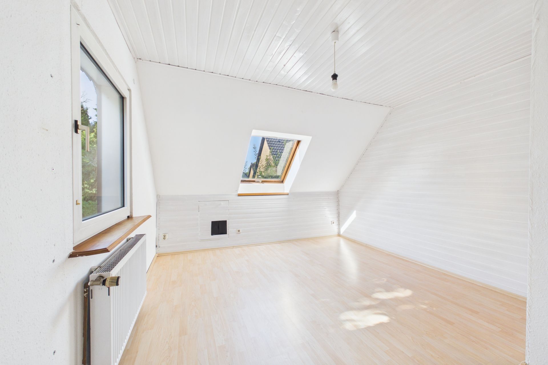 Helles, leeres Dachgeschosszimmer mit Holzfußboden, Fenster und Dachfenster.