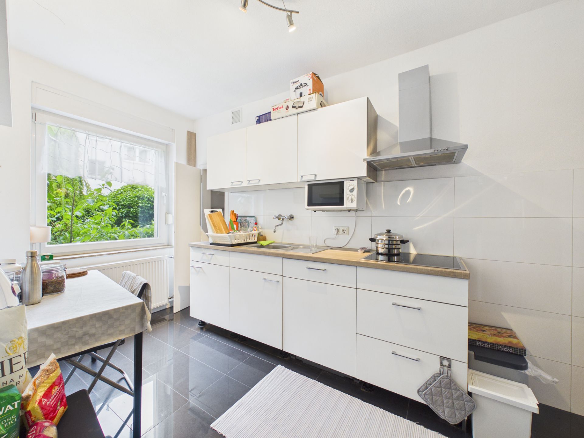 Helle Küche mit weißen Schränken, Esstisch, Fenster und modernen Geräten.