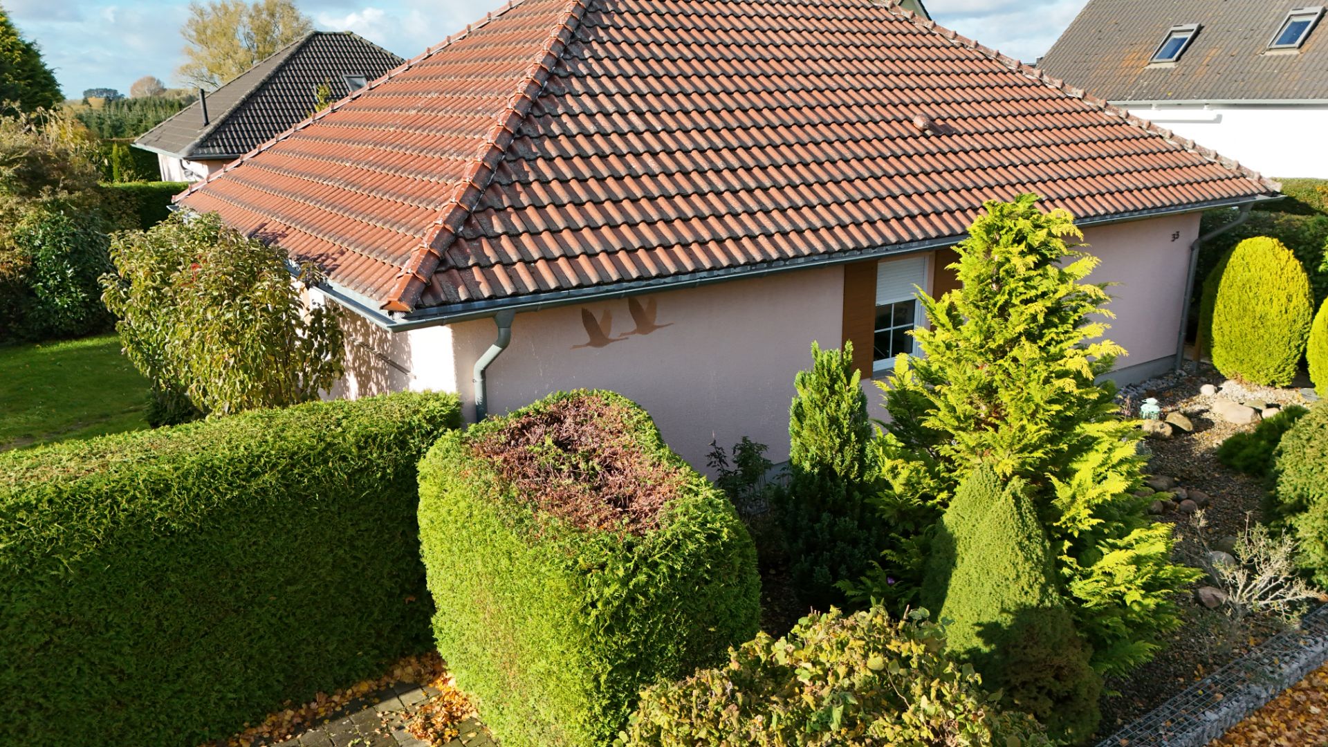 Einfamilienhaus mit rotem Ziegeldach, gepflegtem Garten und verschiedenen Büschen und Bäumen.