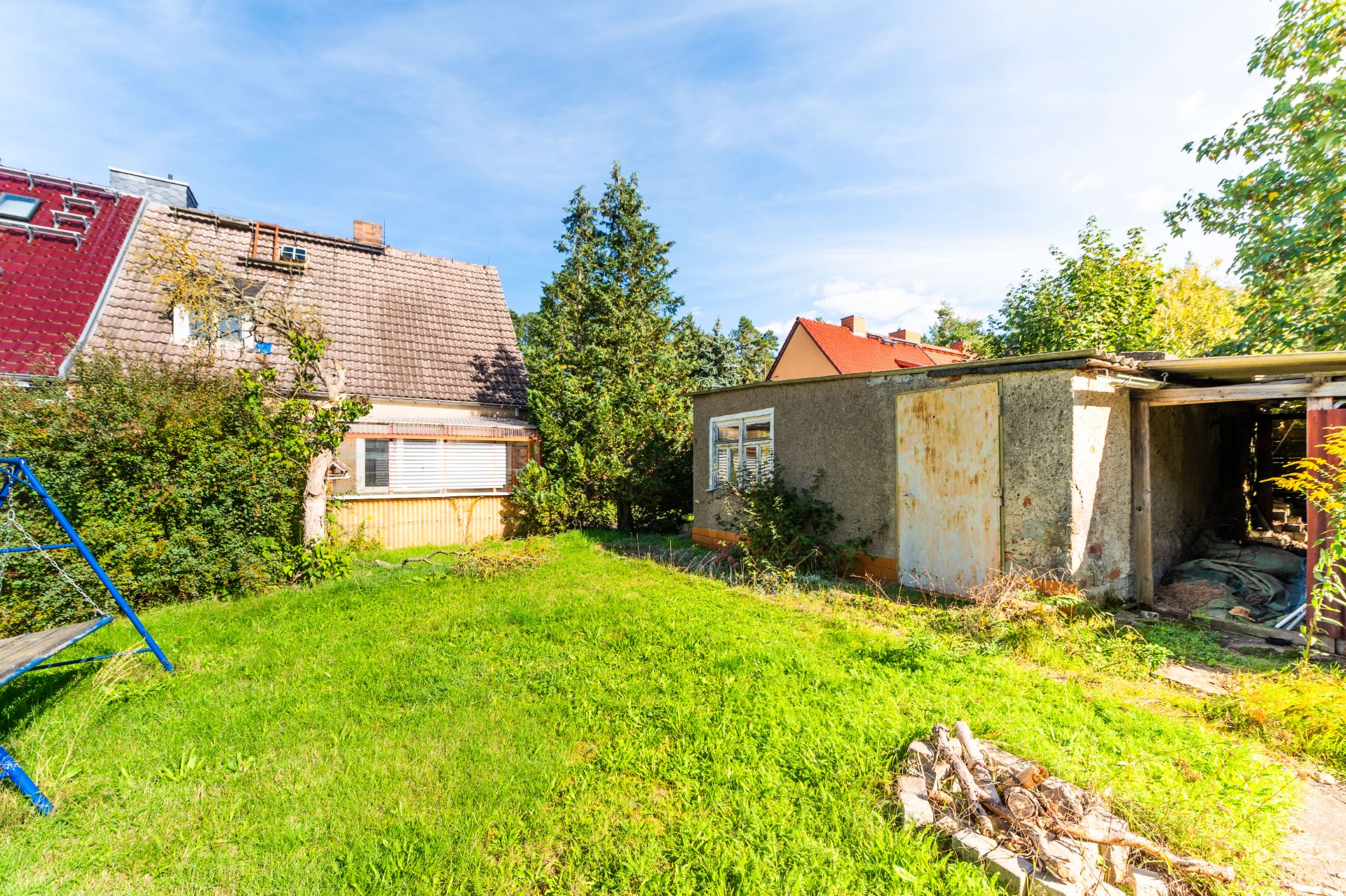 Grüner Garten mit einem Haus, einem alten Nebengebäude und Bäumen im Hintergrund.