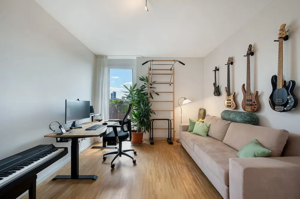 Helles Wohnzimmer mit Sofa, Schreibtisch, Computer, Kletterwand und Gitarren an der Wand.