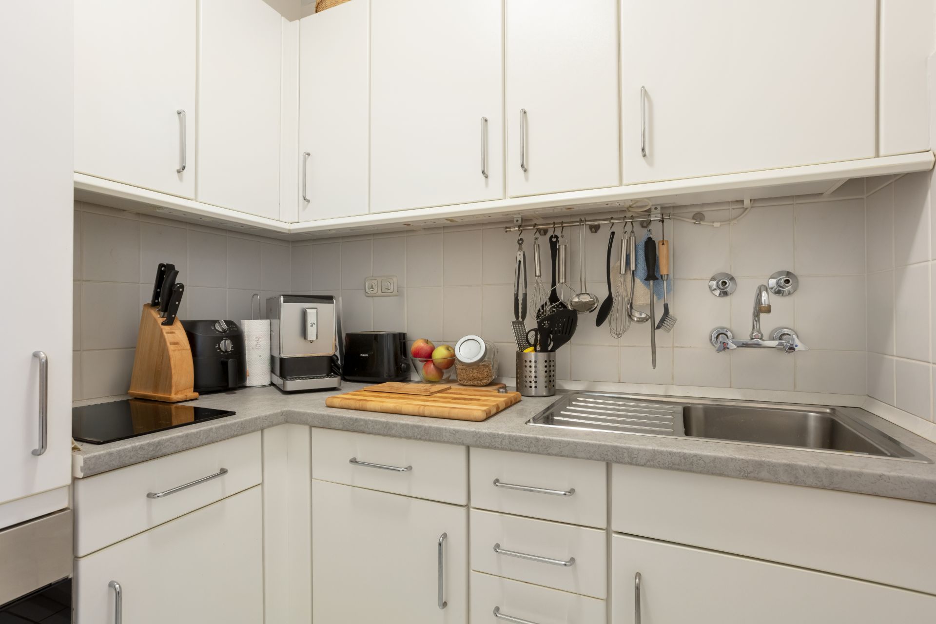 Moderne Küche mit weißen Schränken, Spüle, Kochfeld und Küchenutensilien an der Wand.