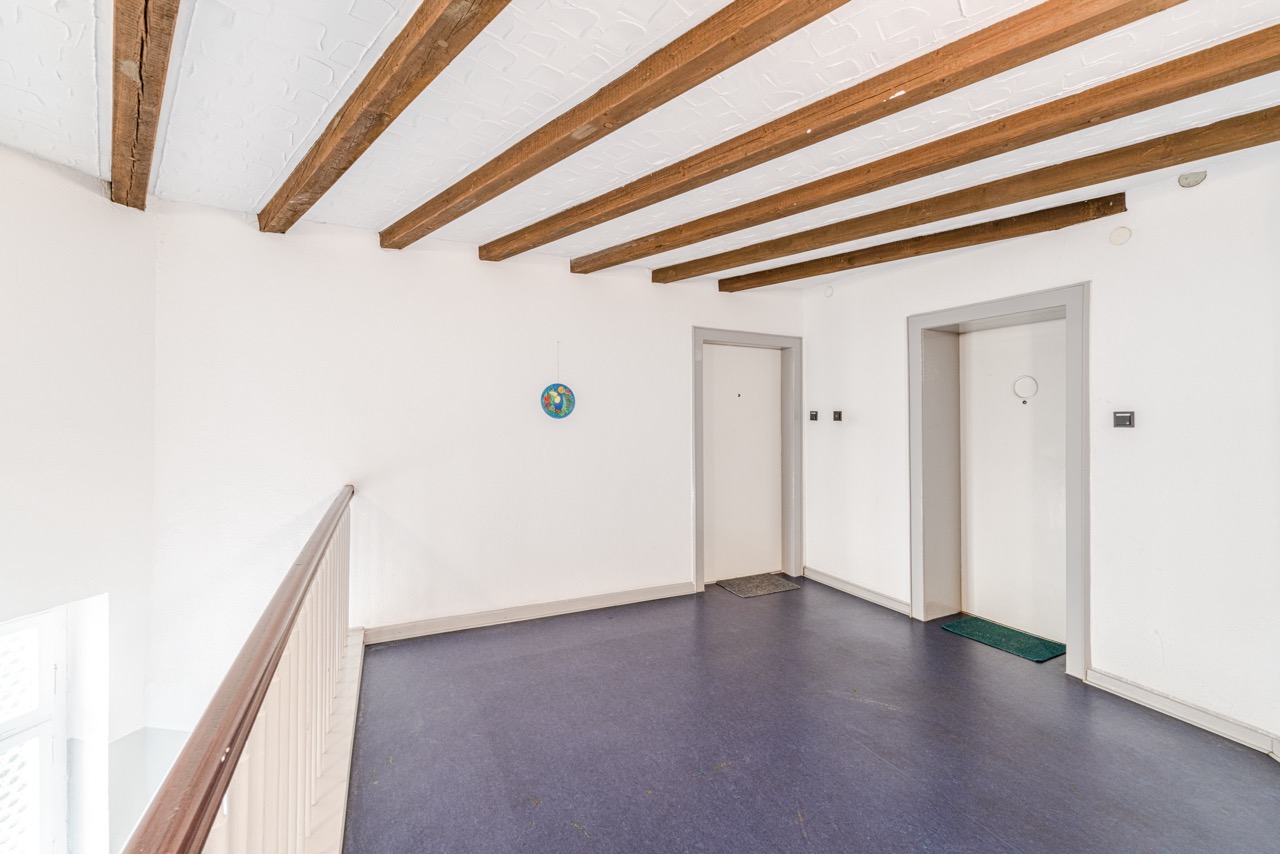 Heller Hausflur mit Holzbalkendecke, zwei weißen Türen und blauem Boden.