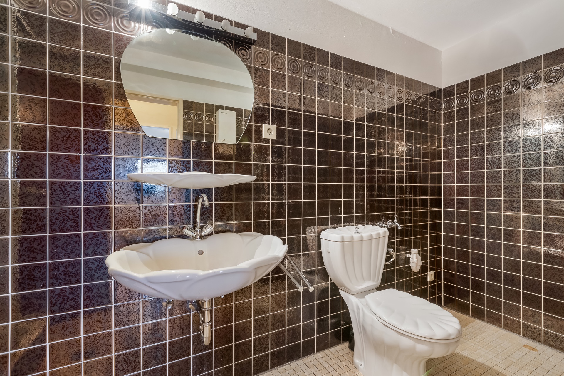 Badezimmer mit braunen Fliesen, weißem Waschbecken und Toilette im Muscheldesign.