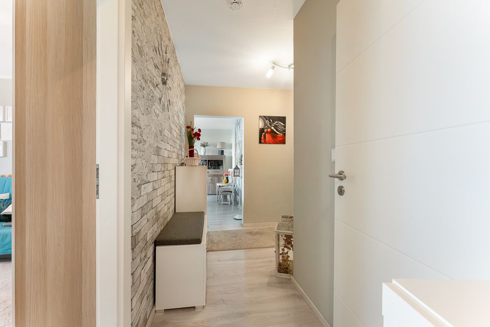 Heller Flur mit Steinwand, Sitzbank und Blick in ein Wohnzimmer mit Esstisch.