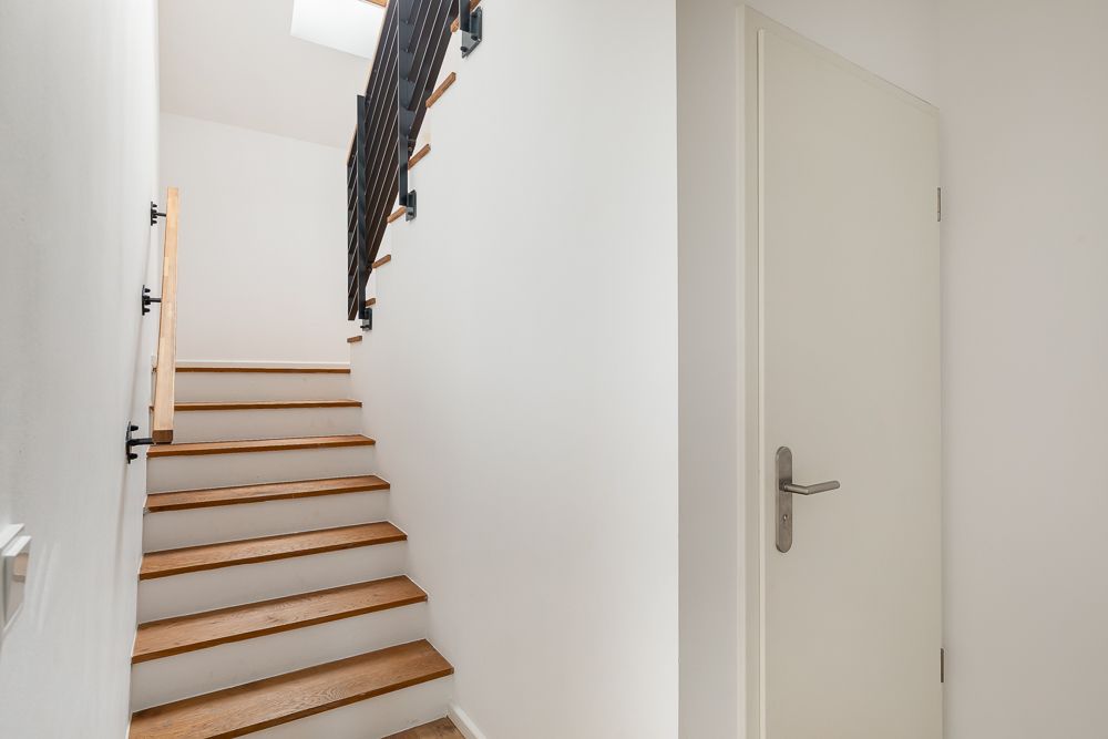 Holztreppe mit schwarzem Geländer neben einer weißen Tür in einem Flur.