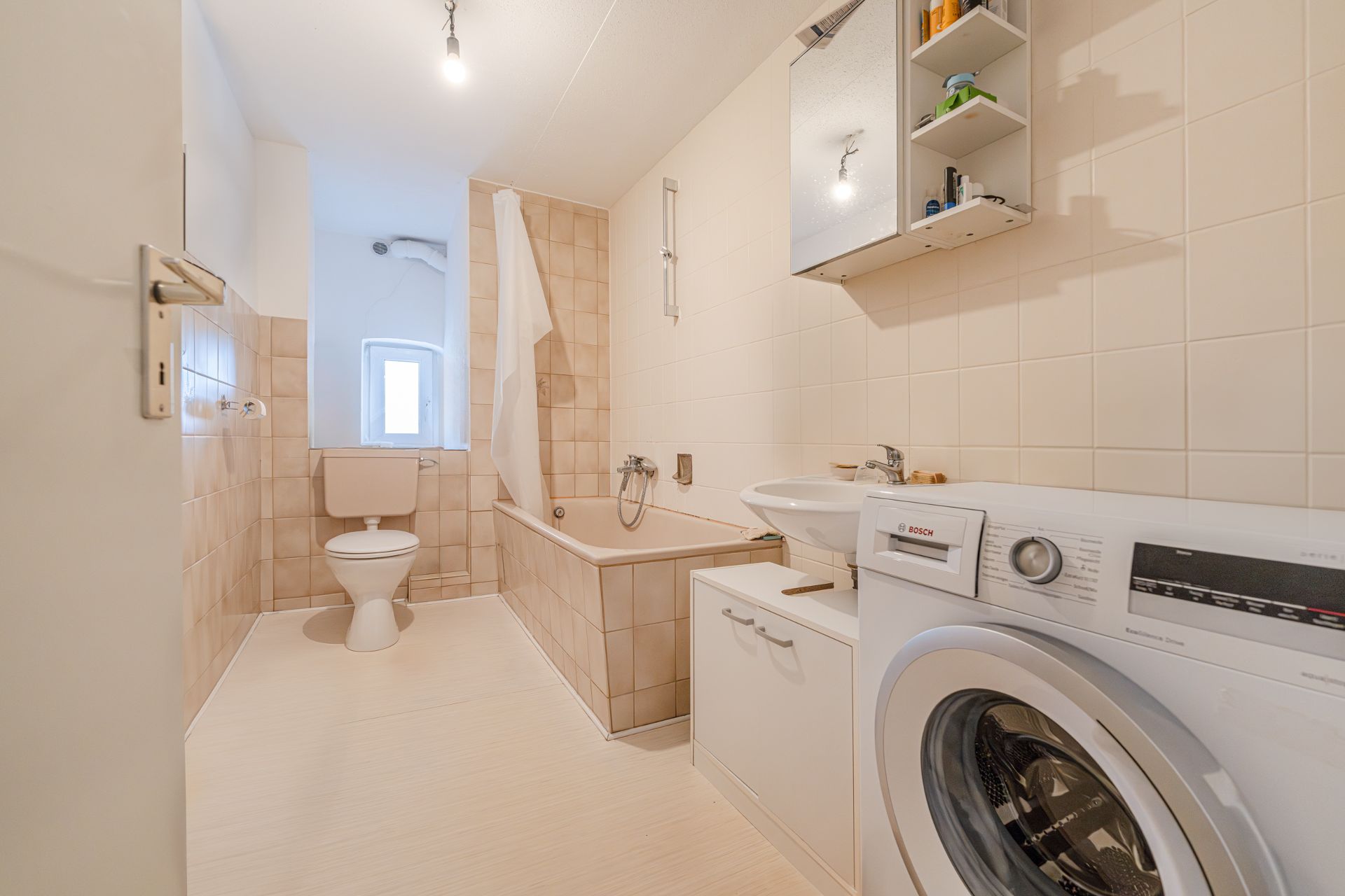 Helles Badezimmer mit Badewanne, Toilette, Waschbecken, Waschmaschine und Spiegelschrank.