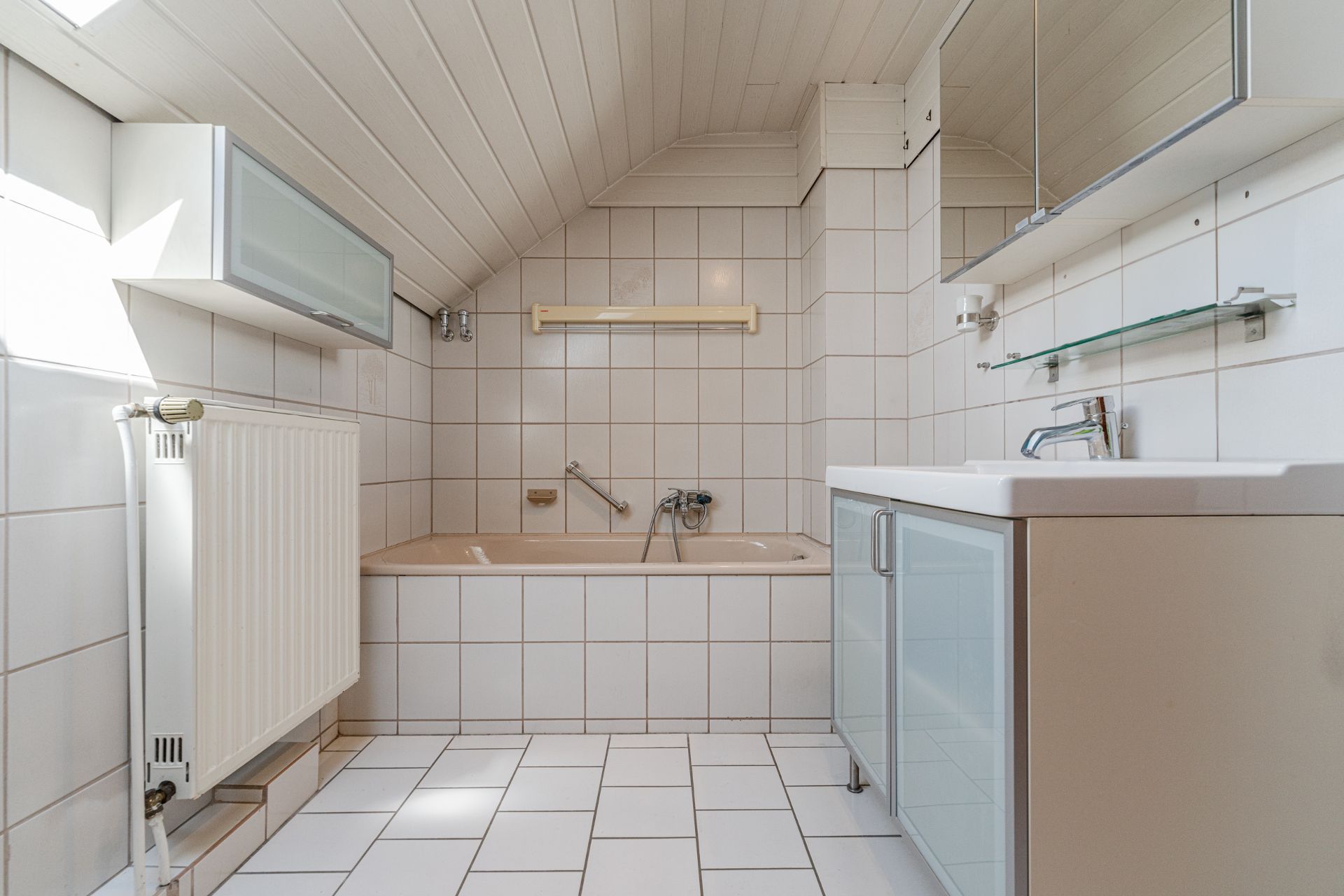 Helles Badezimmer mit Badewanne, Waschbecken, Spiegelschrank und schräger Decke.